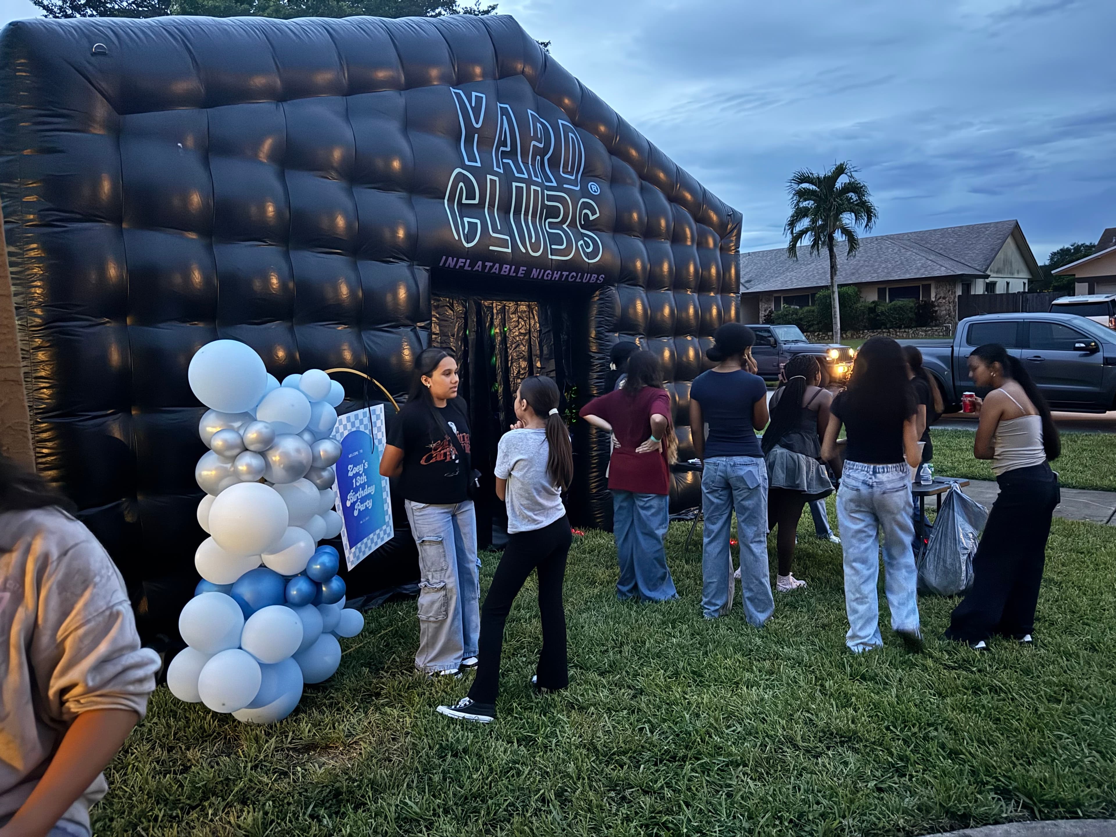 Guests lining up at dusk outside a Yard Clubs nightclub, its neon sign lit
